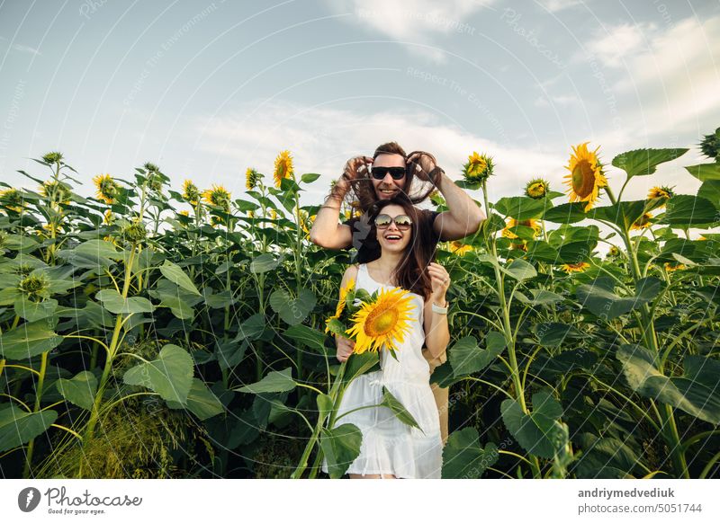 Beautiful couple in sunglases having fun in sunflowers field. A man and a woman in love walk in a field with sunflowers, a man hugs a woman. selective focus