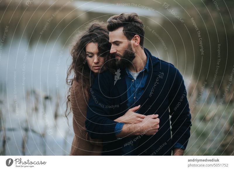 two caucasian lovers near the lake. Young couple is hugging on autumn day outdoors. A bearded man and curly woman in love. Valentine's Day. Concept of love and family