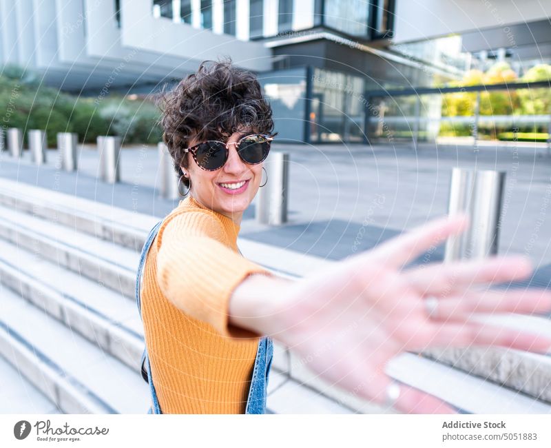 Cheerful woman enjoying sunshine on street building summer carefree cheerful porch free time urban female style city smile positive brunette stair hispanic