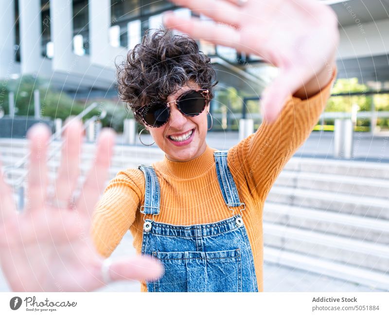 Glad female demonstrating frame gesture near building porch woman carefree photo gesture summer enjoy cheerful street urban style city smile positive brunette