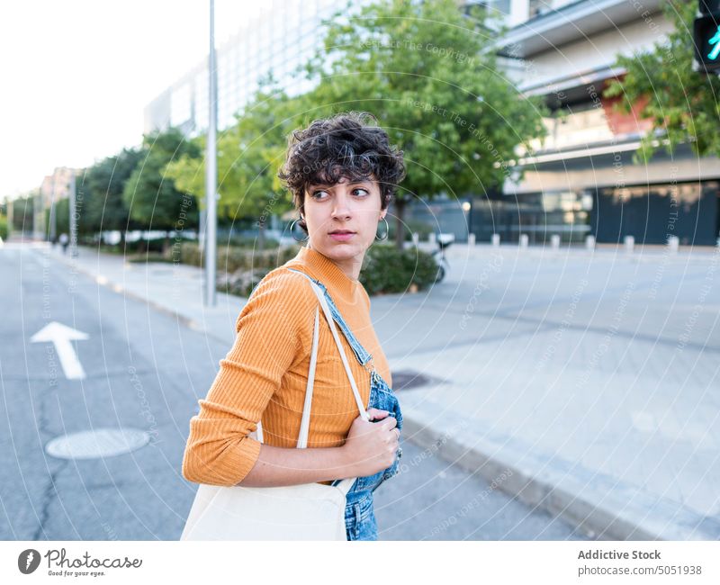 Woman with shopper walking on street woman casual style building road city positive urban young female short hair multistory district modern dark hair