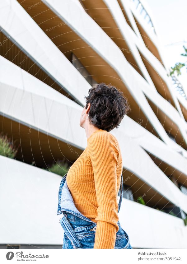 Anonymous woman looking at urban building city admire architecture style street denim construction short hair hairstyle creative contemplate female overall