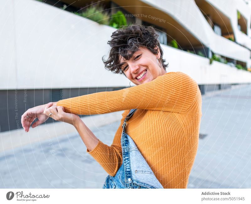 Cheerful woman standing at urban building city architecture style street denim construction short hair hairstyle creative contemplate female overall curly hair