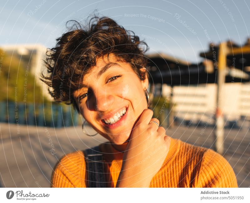 Happy woman standing on sunny street calm sunlight casual shadow city urban smile personality female alone short hair individuality building dark hair young