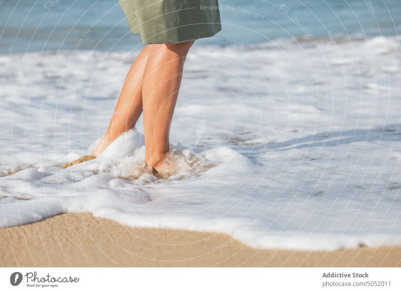 Crop barefoot woman walking along seaside water wave foam beach sand coast shore vacation nature female travel ocean holiday seashore wet splash tourism resort