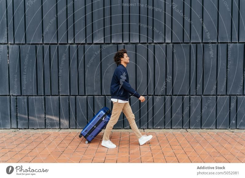 Black man with luggage walking on street tourist suitcase wall pavement building urban pull male black african american ethnic modern holiday bag weekend stroll