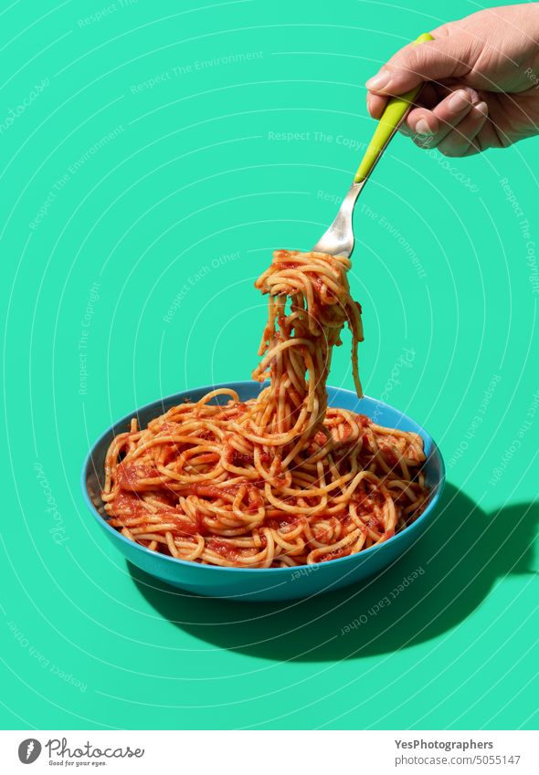 Spaghetti Pomodoro on a fork, minimalist on a green background above blue bowl bright carbs classic color copy space creative cuisine cut out delicious dinner