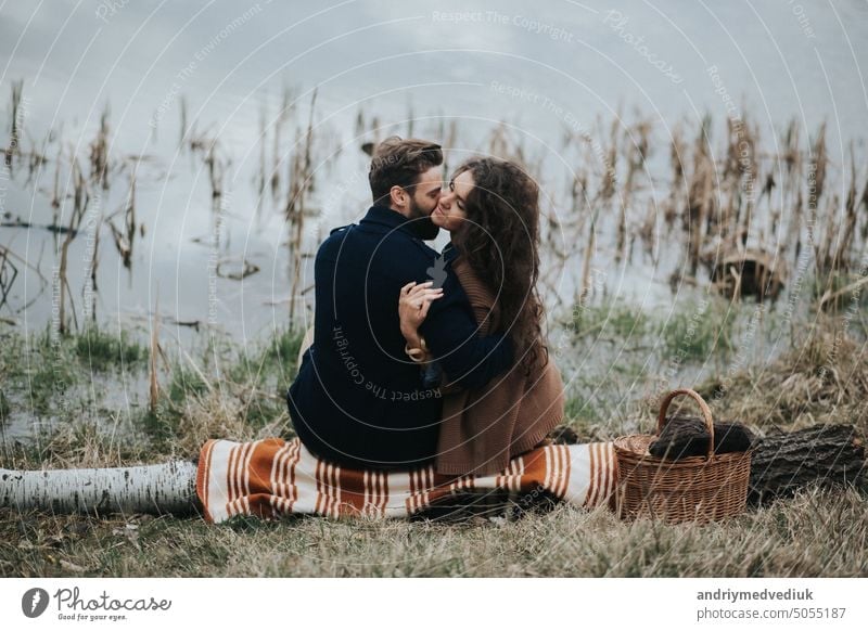 two caucasian lovers sitting on blanket by the lake. Young couple is hugging on autumn day outdoors. A bearded man and curly woman in love. Valentine's Day. Concept of love and family. back view