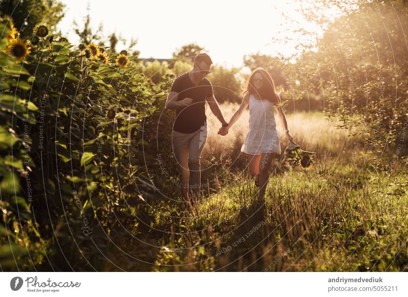 Beautiful couple having fun in sunflowers field. A man and a woman in love walk in a field with sunflowers, a man hugs a woman. selective focus beautiful summer