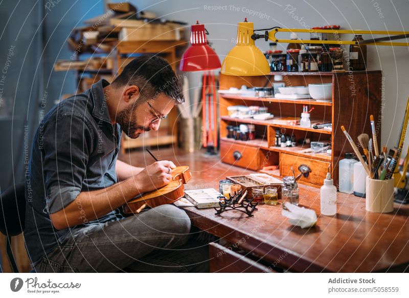 Focused luthier varnishing violin in workshop craftsman polish artisan master professional wooden instrument handicraft tool skill color manufacture woodwork