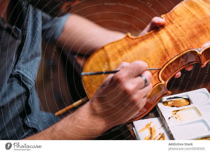 Focused luthier varnishing violin in workshop craftsman polish artisan master professional wooden instrument handicraft tool skill color manufacture woodwork