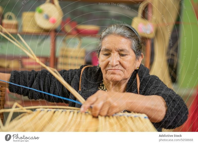 Senior Hispanic woman crafting grass basket craftswoman weave focus dry handmade table pensioner wicker basketry female elderly senior aged hispanic ethnic
