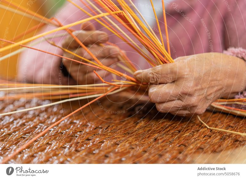 Anonymous elderly woman weaving basket from grass craftswoman weave straw table wicker handmade handicraft natural material basketry female senior aged wrinkle