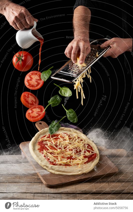 Crop chefs cooking pizza with tomatoes in dark studio cheese grate margherita basil recipe pour fall marinara ingredient food photography advertise culinary