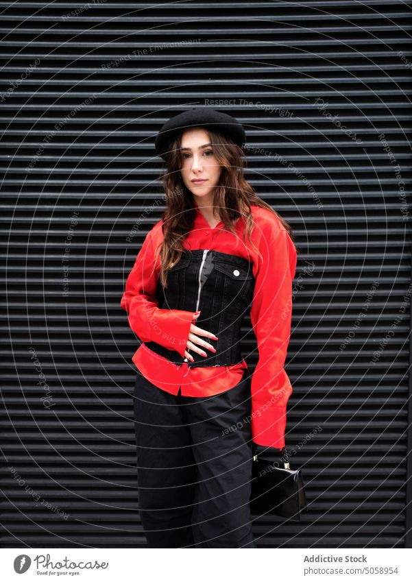 Stylish brunette standing on black wall woman style street appearance outfit female young individuality daytime urban long hair building carefree charismatic