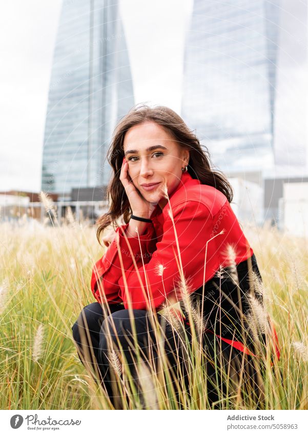 Stylish woman sitting in grass in park style urban city lean on hand haunch summer weekend female young lawn brunette daytime lifestyle personality season