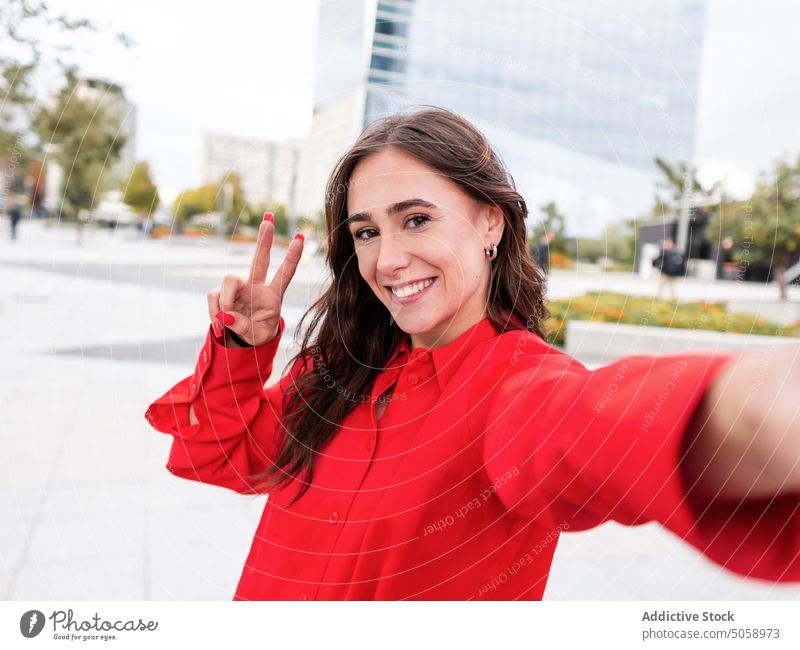 Happy stylish female taking selfie on street woman smile happy v sign gesture urban style brown hair young long hair cellphone two fingers self portrait
