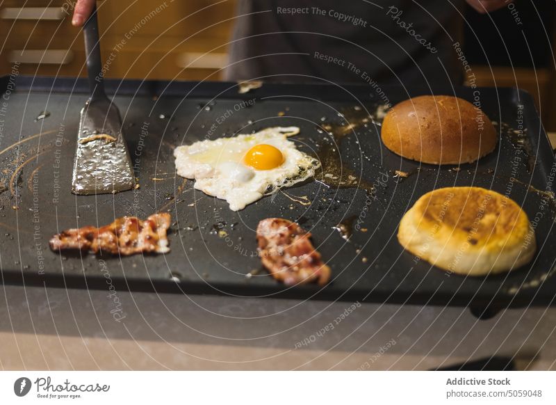 Crop man cooking burger on electric grill chef fry kitchen prepare spatula ingredient process delicious food culinary cheese bacon bun egg male apron meal