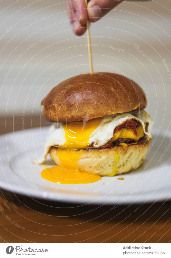 Delicious fresh made burger on plate person hamburger delicious scrumptious toothpick egg bun food fast food serve table tasty meal dish yummy appetizing lunch