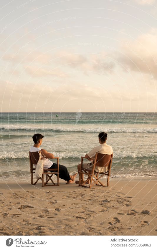 Anonymous men sitting on chairs near sea friend beach admire ocean nature endless vacation wavy together enjoy water horizon summer friendship peaceful shore
