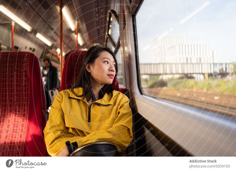 Asian woman riding train in city ride window passenger travel commute daytime public london england uk united kingdom female young transport trip railroad