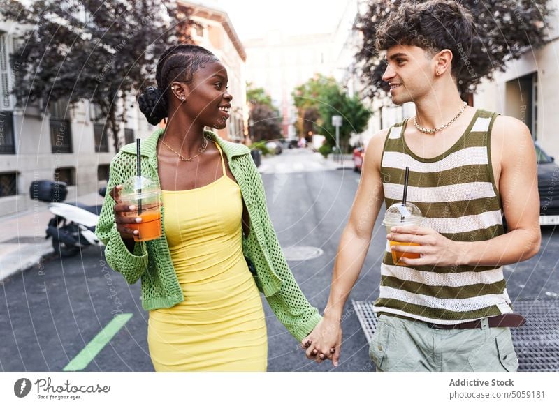 Loving young multiethnic couple holding hands and drinking juices while walking on street smile relationship romantic love together takeaway city multiracial