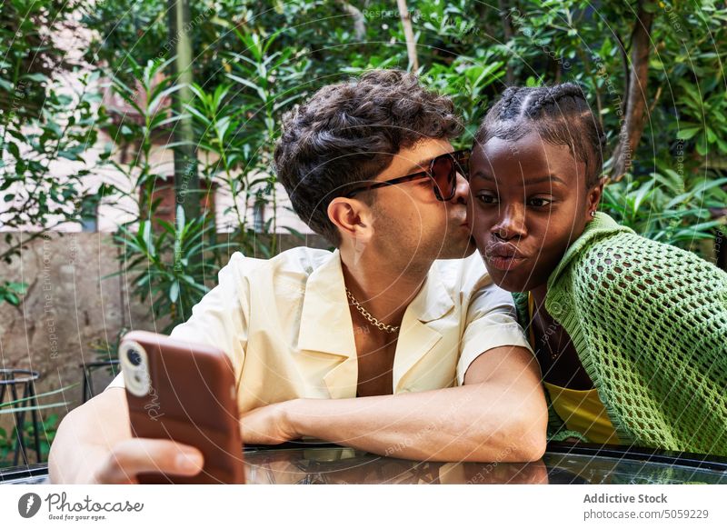 Diverse couple taking selfie in garden smartphone kiss date pouting lips together love summer girlfriend boyfriend cheek diverse multiethnic multiracial black
