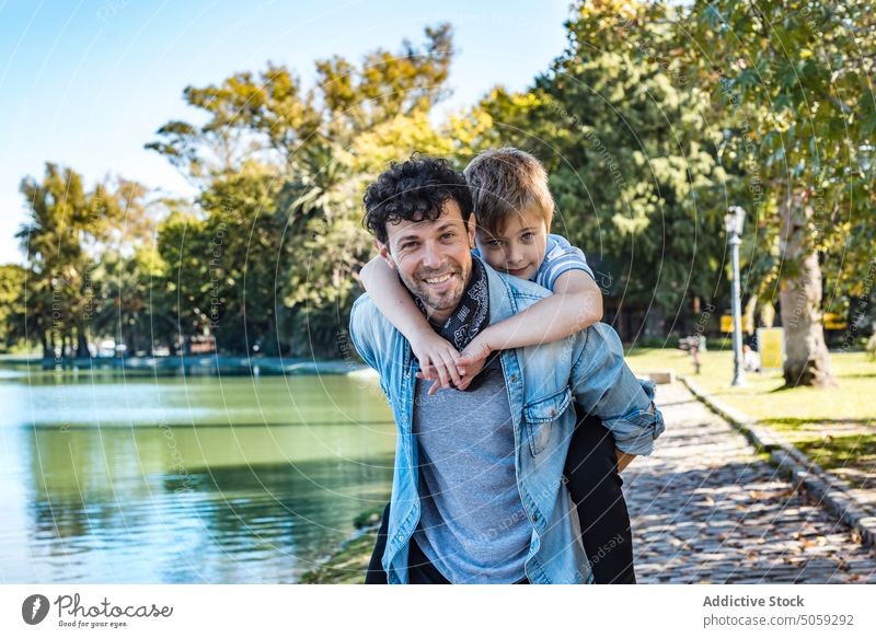 Father with son near lake in park father piggyback ride smile autumn weekend together man boy happy love path childhood glad carry relationship casual daytime