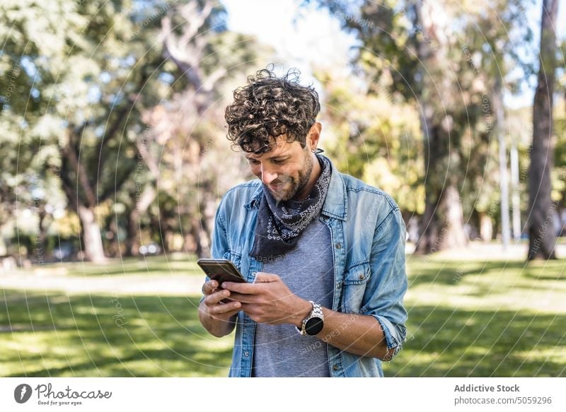 Man browsing smartphone in park man watching weekend summer lawn phone call daytime conversation male connection casual mobile gadget device cellphone