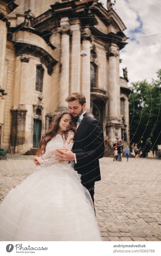Stylish bride and groom gently hugging on european city street. Gorgeous wedding couple of newlyweds embracing near ancient building. romantic sensual moment of newlyweds