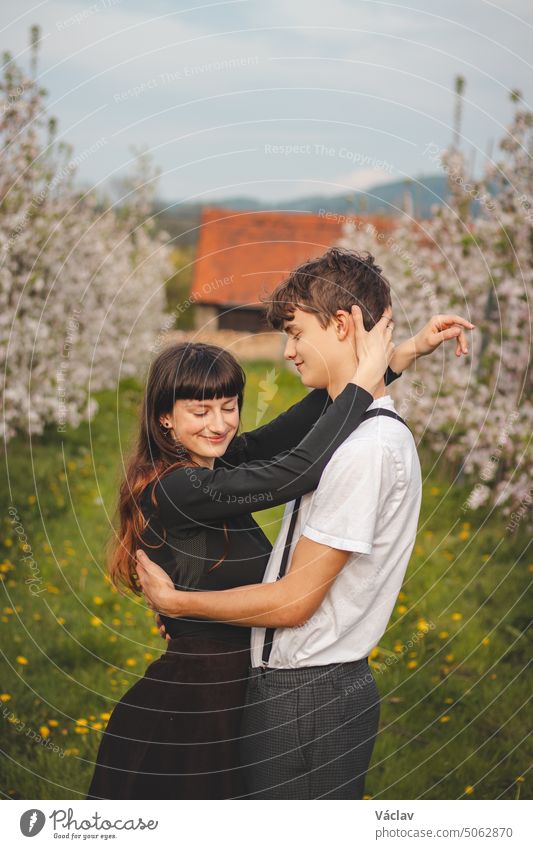 Young strong love between two young people walking under apple trees. Candid portrait of a couple in casual clothes. Affection of two people relationship