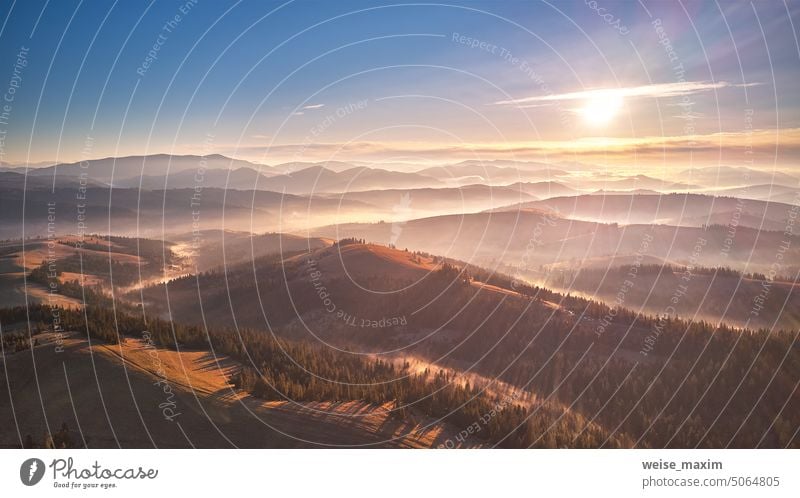 Mountain autumn Sunrise. Majestic Morning fog, Beautiful tonal perspective. Fall sunny Landscape, misty forest on hills. Majestic aerial scenery of valley