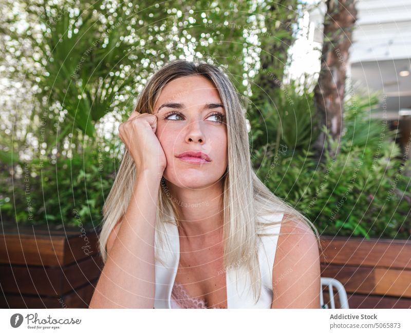Thoughtful female sitting on terrace woman lean on hand think summer blond thoughtful bored weekend daytime young adult contemplate individuality personality