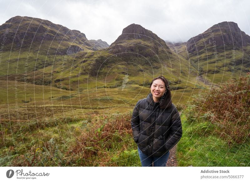 Cheerful Asian tourist against mountains in valley woman smile happy outerwear cloudy nature highland glen coe scotland uk united kingdom female asian ethnic