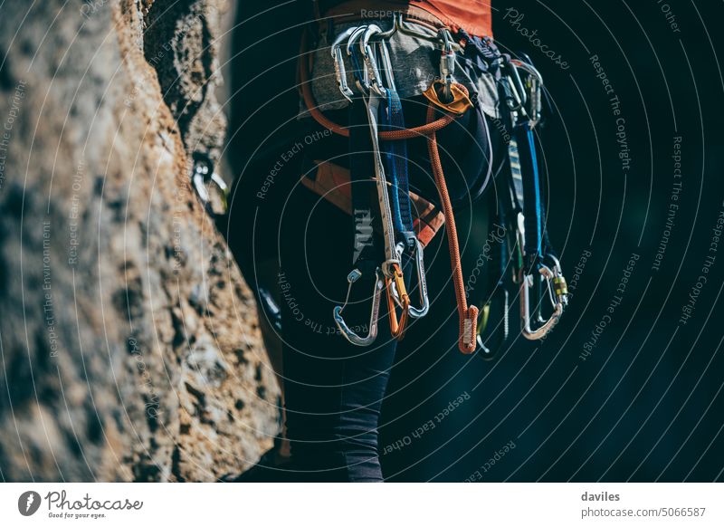 Detail of climb gear and equipment attached to a woman climbing harness while she climbs a route activity adventure alpinism aluminum belaying carabiner carbine