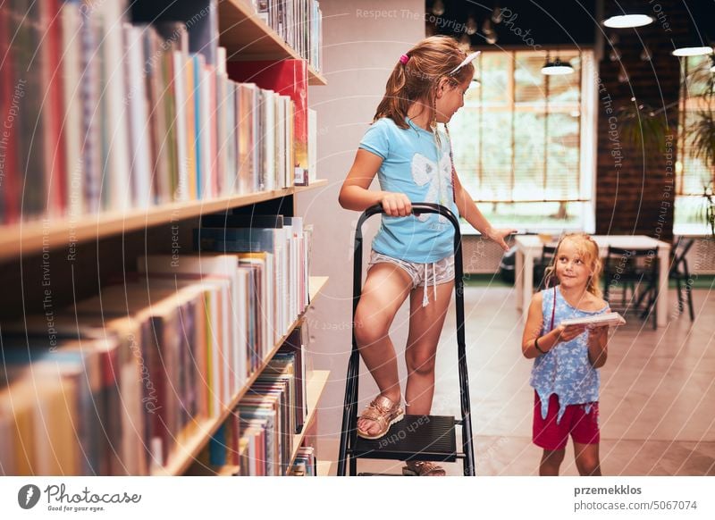 Two schoolgirls spending time in school library. Primary school students learning from books. Children having fun in school club. Doing homework back studying
