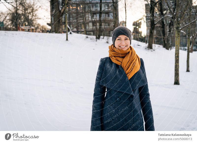 Smiling woman in a winter coat, scarf and cap against the background of a snowy city Woman Winter Cold Snow Happiness Happy Joy people person more adult Coat