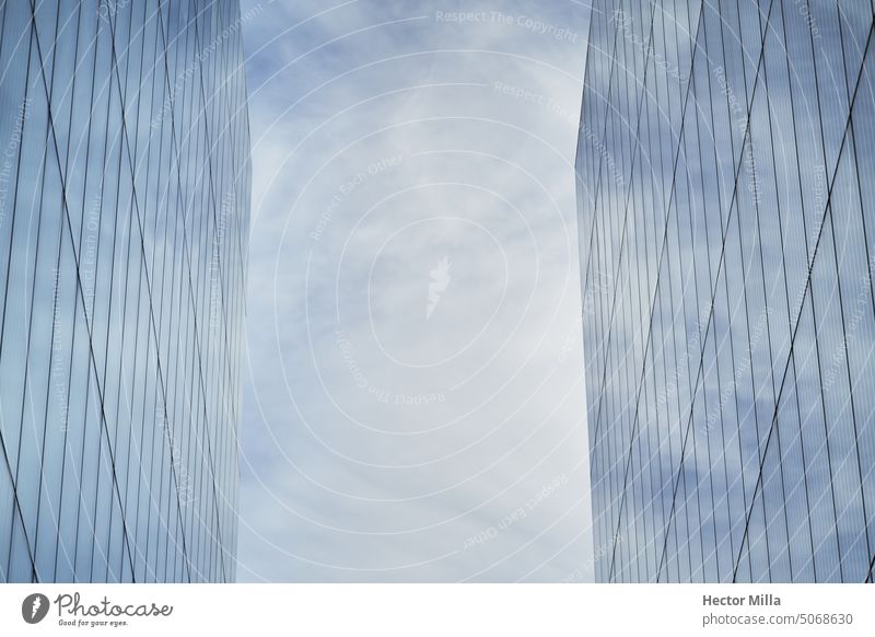 Two glass facade buildings with a geometric structure that reflect the sky with clouds with a minimalist and monochrome look Building minimalism Blue sky Glass
