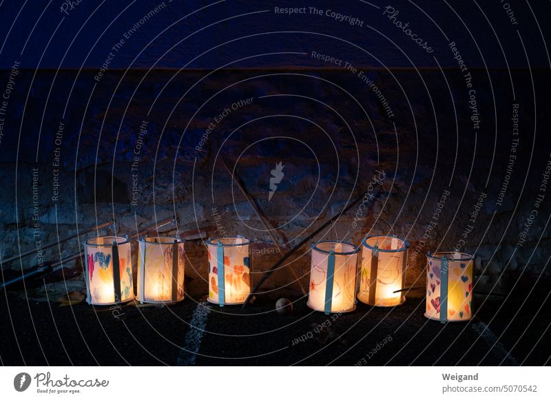 Glowing paper lanterns for St. Martin's procession in November placed in a row on the ground in front of a stone wall in the dark of night Night Light lit