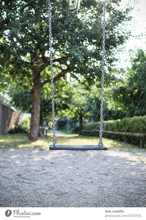 Lonely swing on playground in front of tree and green hedge Swing To swing Past Abuse Playground forsake sb. Deserted children's playground Dark