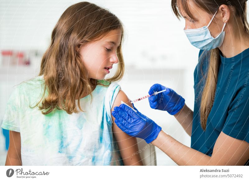 Female nurse with surgical mask and in gloves giving vaccine injection to a teenager in clinic. Children vaccination. antibiotic arm booster care child disease