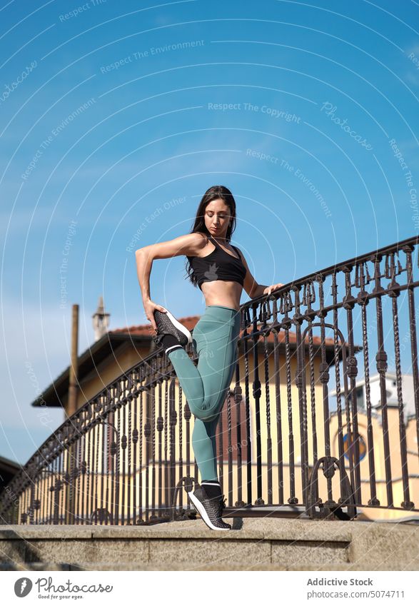 Slim woman stretching legs leaning on railing exercise training workout staircase sport fitness sportswoman jogger runner athlete strength focus sporty strong