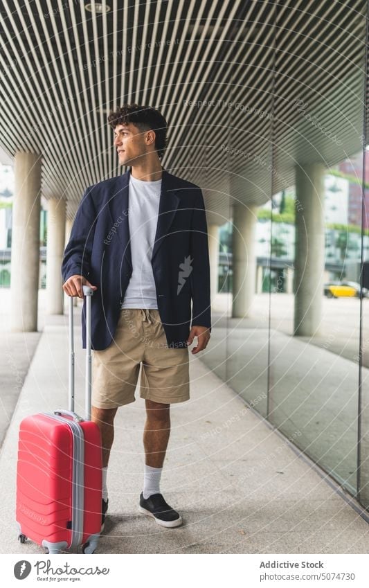 Young man with suitcase on street smile building airport traveler glass wall trip weekend male young smart casual baggage tourist style tourism daytime