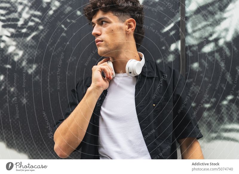 Male meloman adjusting headphones on neck wall street urban style touch ornament male young casual modern summer wireless palm leaf headset curly hair dark hair