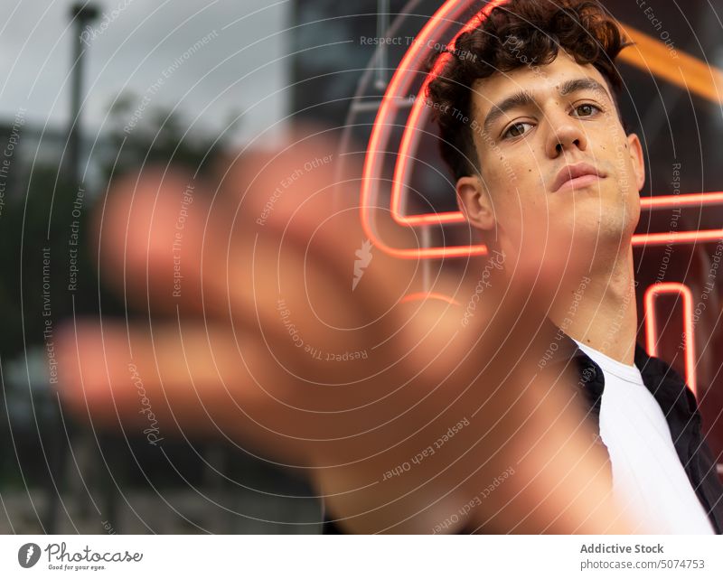 Young male reaching out to camera man reach out street urban sign neon glass wall appearance illuminate style young dark hair brown eyes restaurant curly hair