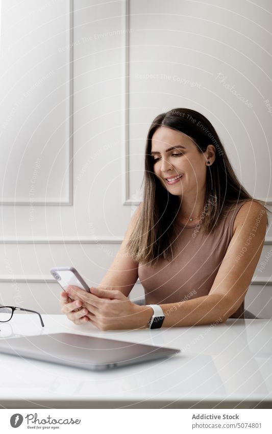 Happy businesswoman using smartphone in modern light office message entrepreneur positive work smile laptop workspace connection female adult brunette