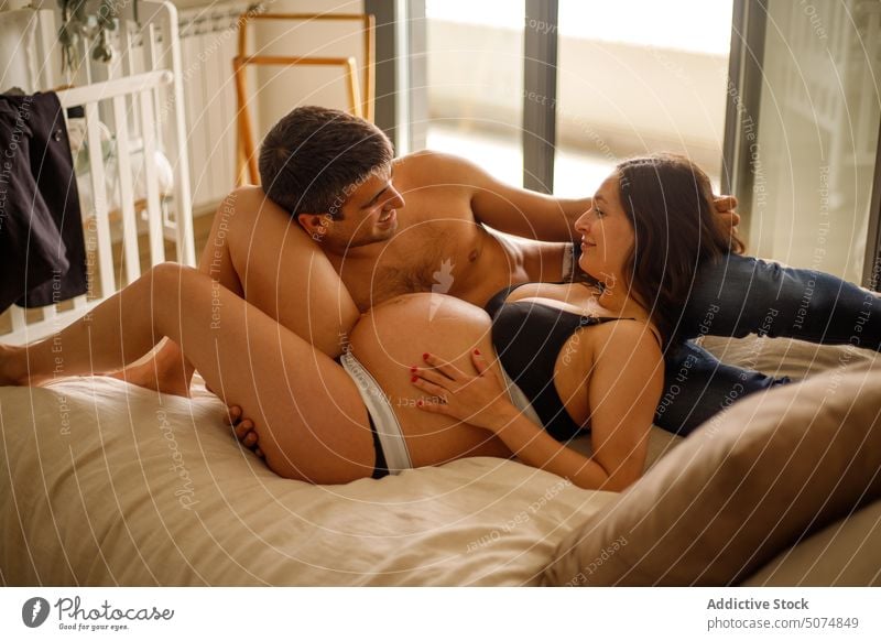 Man caressing pregnant woman belly in bedroom couple husband wife pregnancy underwear shirtless relationship lying love maternal together mother expect parent