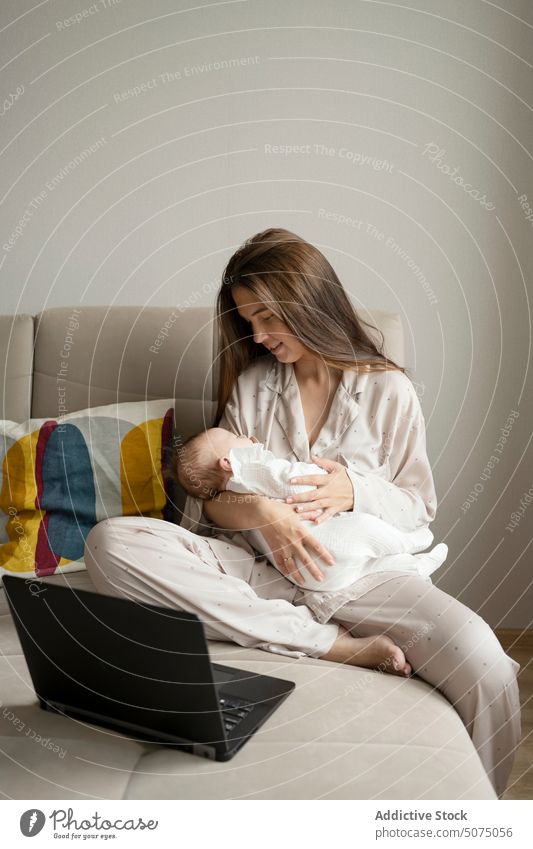 Mother with baby using laptop on sofa mother freelance hug living room home project woman young infant newborn remote embrace internet device gadget together