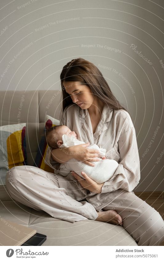 Young mom caressing sleeping infant mother baby hug sofa living room home love morning female young tender peaceful pajama fondness parent together newborn