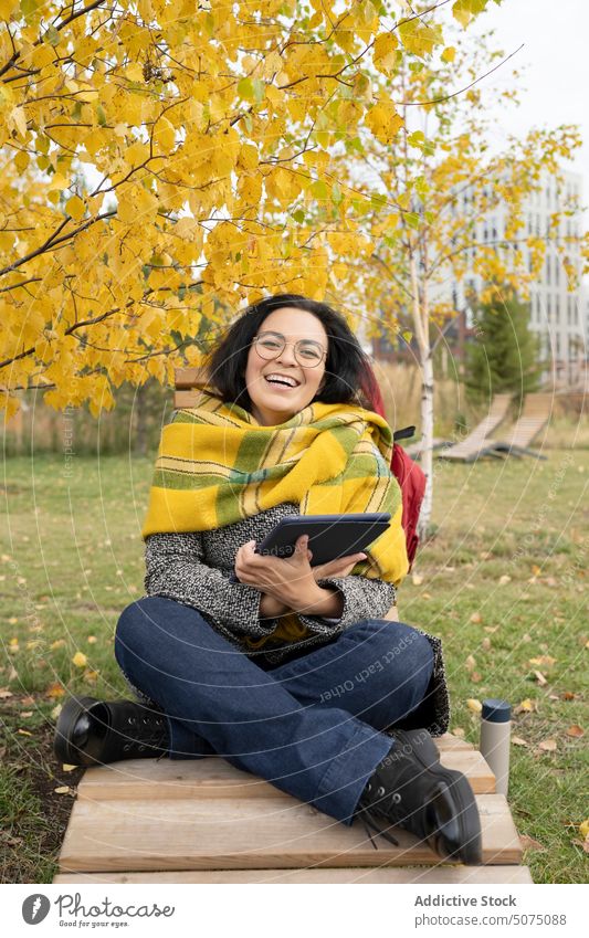 Cheerful woman with tablet PC in park freelance digital using autumn bench blanket browsing gadget happy female device cheerful social media young smile wrap